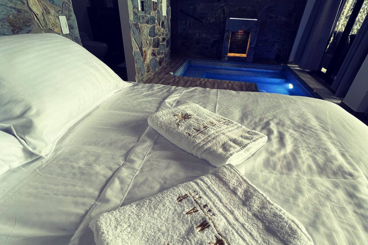 A hotel room with a bed, a stone wall, and a neon sign.