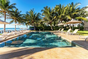 A swimming pool with lounge chairs and umbrellas, surrounded by palm trees and a view of the ocean. - Aparthotel Eeb Ti Kaan Tulum - Luxury Condos. (Tulum)