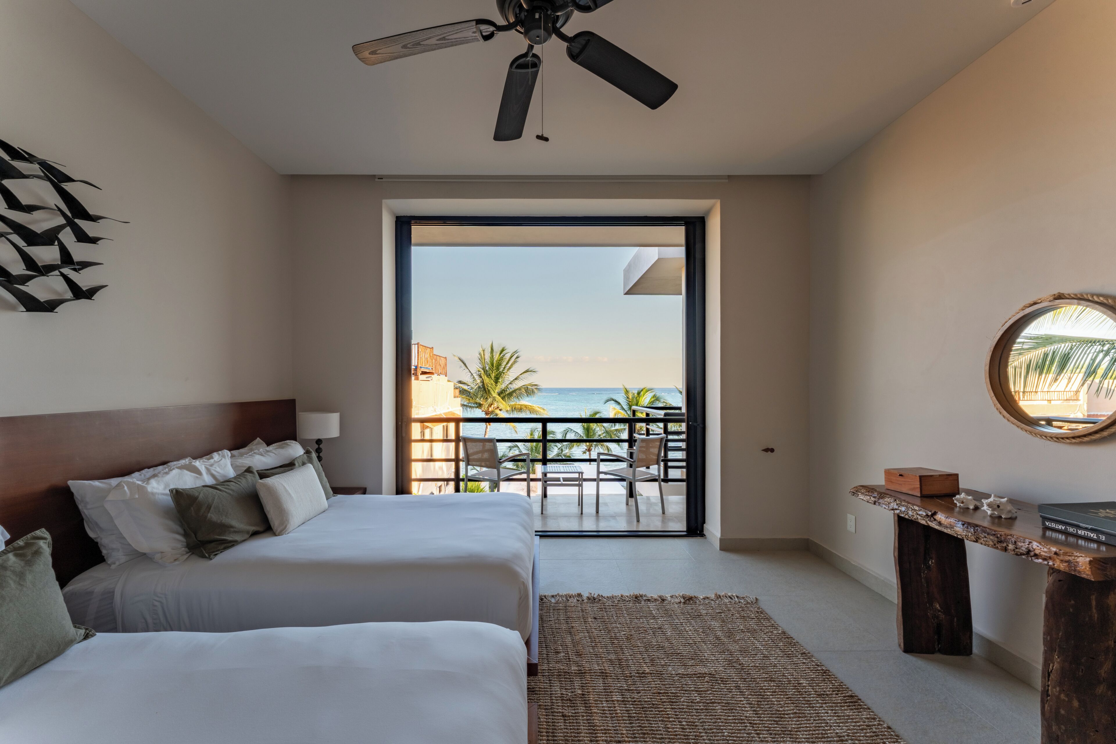 Une chambre avec un lit, un ventilateur de plafond, une vue sur l’océan et un balcon équipé de chaises.