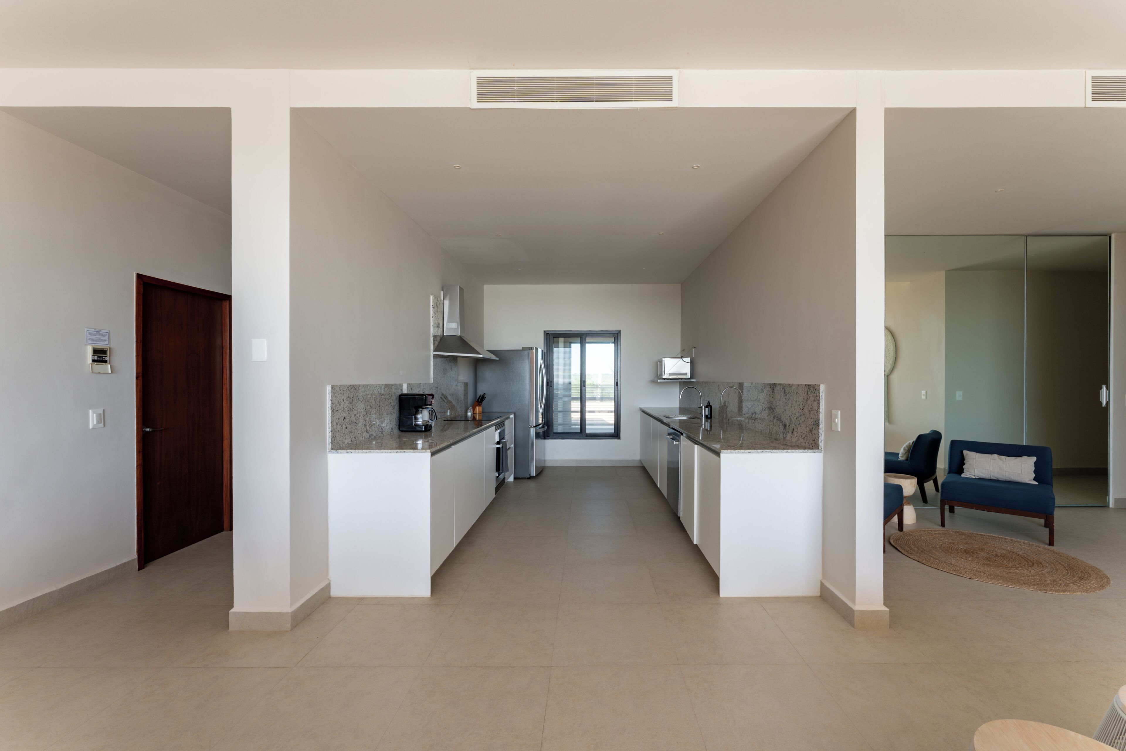 A modern kitchen with a central island, a dining area with a sofa, and a view to the living room.