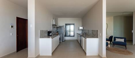 A modern kitchen with a central island, a dining area with a sofa, and a view to the living room.