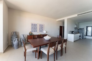 A modern dining area with a wooden table and chairs, a kitchen in the background, and decorative vases on the floor. - Aparthotel Eeb Ti Kaan Tulum - Luxury Condos. (Tulum)