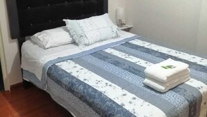 Una cama bien hecha con una colcha a rayas, un cabecero negro y una mesita de noche pequeña con una lámpara.