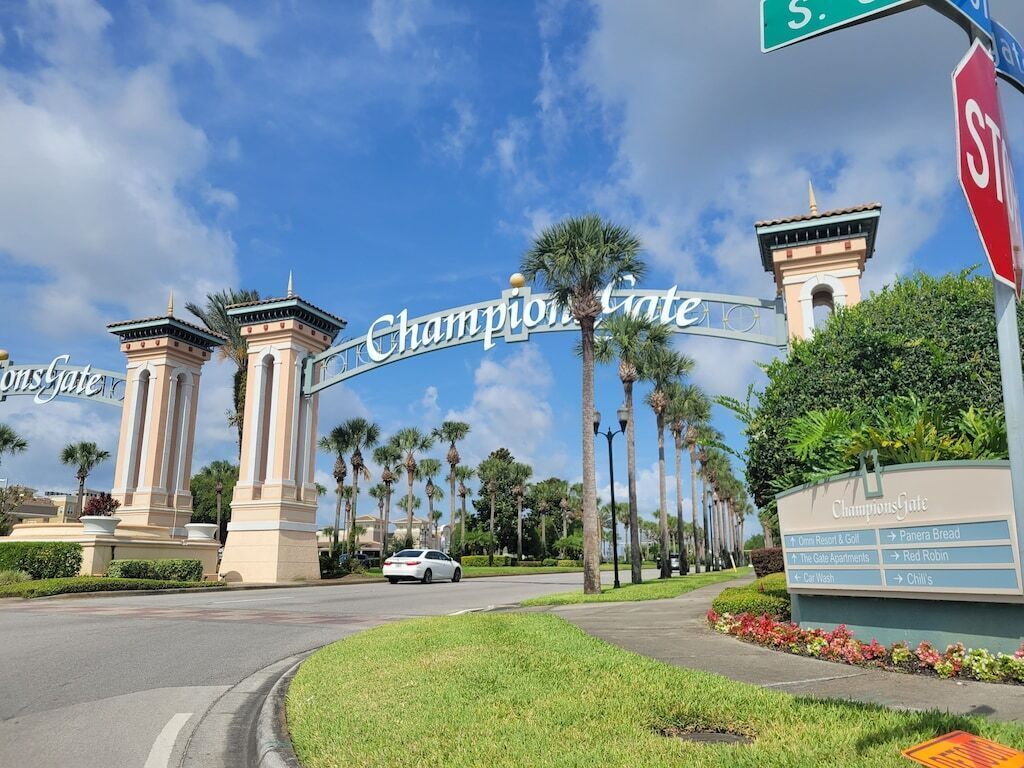 The entrance to ChampionsGate with a clear view of the sign, palm trees, and a road leading to the property.