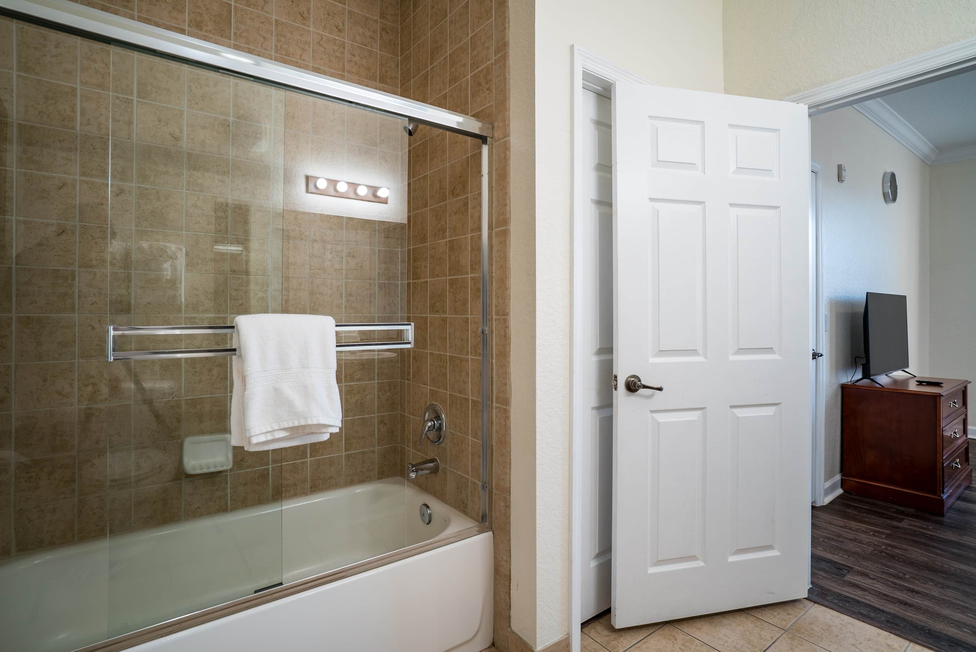 A bathroom with a glass-enclosed shower, a white bathtub, and a white door leading to another room.