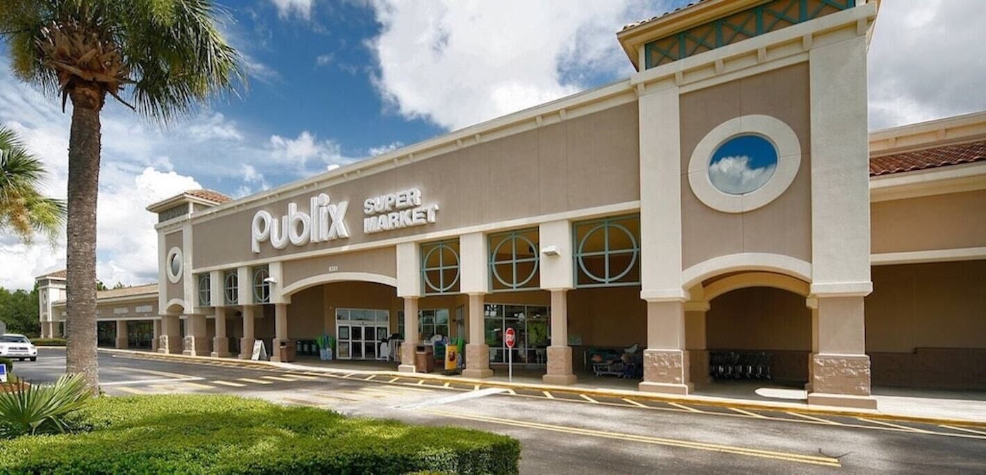 Un supermarché Publix à l’architecture moderne, avec de grandes fenêtres et un palmier au premier plan.