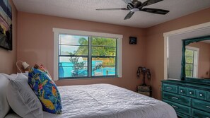 A bedroom with a bed, a window with blinds, a ceiling fan, a dresser, and a wall clock.