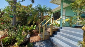 A tropical garden with a wooden staircase leading to a green building with a covered porch.