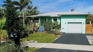 A single-story house with a green exterior, a front porch, and a driveway leading to a garage.