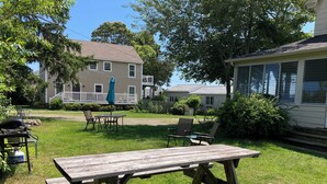 A wooden picnic table in a grassy backyard with a porch and a covered patio area in the background. - 2-Bedroom Apt Near Hampton Beach (Hampton)