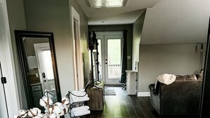 Een eethoek met een houten tafel en stoelen, een vaas met witte bloemen, en een uitzicht op de keuken en woonkamer door een open deur.