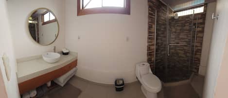 Een badkamer met een ronde spiegel, een wastafel, een toilet en een douche.