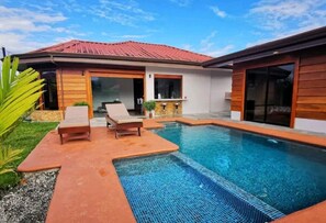 Une maison moderne dotée d’une piscine, d’une terrasse avec des chaises longues et d’un toit recouvert de tuiles.