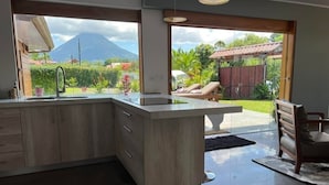 Une cuisine moderne dotée d’un grand îlot central, d’un évier et donnant sur un jardin avec une chaise et une table.