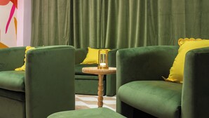 Un juego de sofá verde con almohadones amarillos, una mesita de madera pequeña y un reposapiés verde.