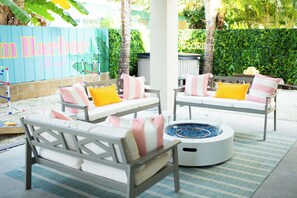Un patio con dos sofás blancos con cojines rosa y amarillos, una mesa redonda con un brasero azul y una alfombra a rayas.