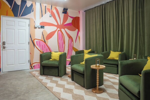 A room with green sofas, yellow cushions, a patterned rug, and a colorful abstract wall.