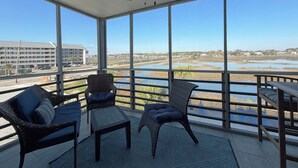 A balcony with wicker furniture, a ceiling fan, and a view of a water body and buildings. - Marshside Inn 201 - Second Row (Marshfront) in Garden City Beach (Garden City)