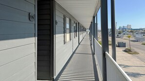 A corridor with a series of doors, a clear sky, and a distant cityscape. - Marshside Inn 201 - Second Row (Marshfront) in Garden City Beach (Garden City)