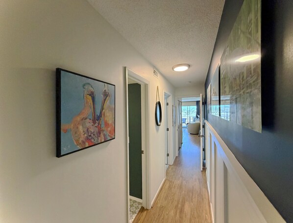 A hallway with a painting, a mirror, and a door leading to a room.