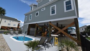 Ein zweistöckiges Haus mit überdachter Terrasse, Schwimmbad und Gartenmöbeln.