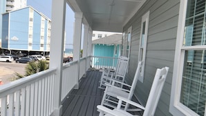 Eine überdachte Veranda mit Holzdeck, weißen Geländern und Schaukelstühlen.