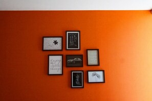 A wall with seven framed items: a puzzle piece, a guitar, sheet music, a car, a camera, a quote, and a dandelion.