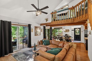 Un vaste espace de vie comprenant un grand canapé en cuir marron, un ventilateur de plafond et un escalier en bois menant à un niveau supérieur.