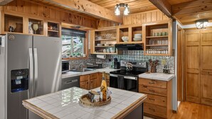 A kitchen with wooden cabinets, a stainless steel refrigerator, a stove, and a tiled backsplash. - 5 Star mountain home where the host thought of everything, so you don’t have to! (Bushkill)