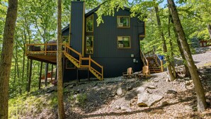 A cabin with a wooden deck, a staircase, and a view of the surrounding forest. - 5 Star mountain home where the host thought of everything, so you don’t have to! (Bushkill)