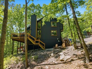 Une cabane dotée d’une terrasse en bois, d’un escalier et offrant une vue sur la forêt environnante.