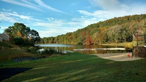 Um lago com um píer, uma área gramada e uma colina arborizada.