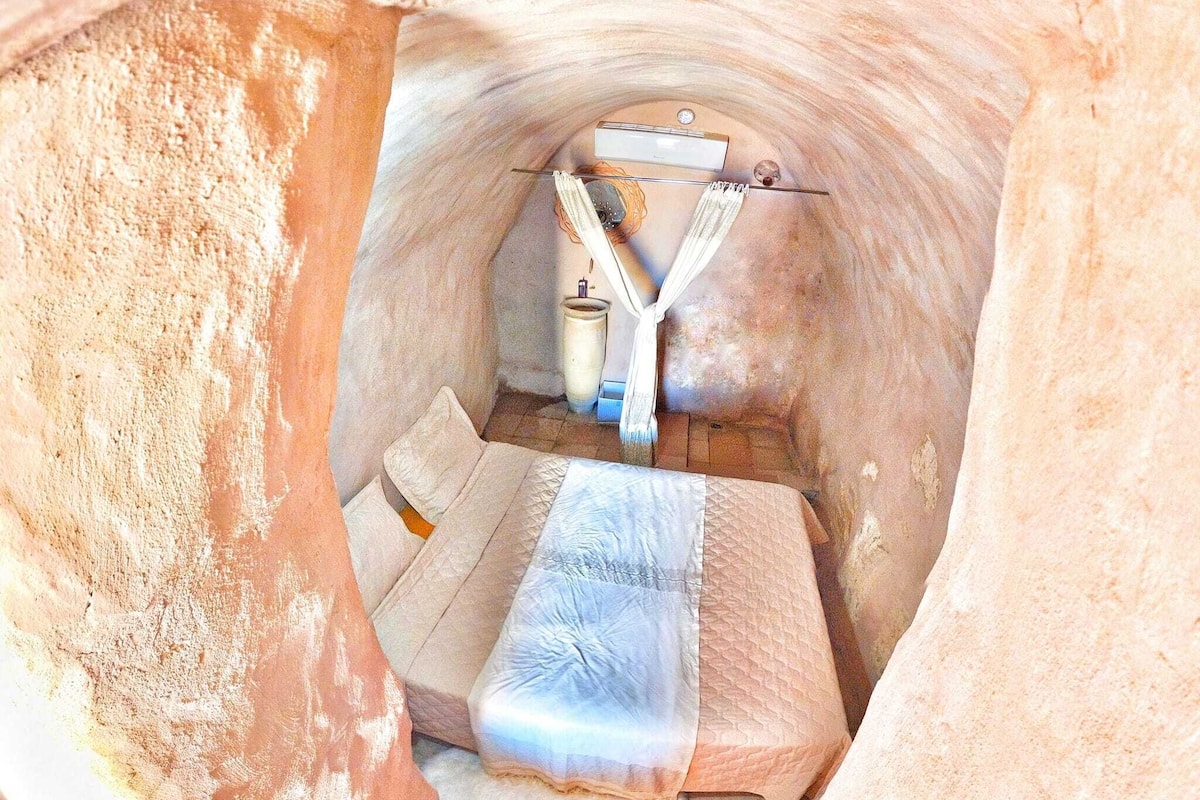 Une petite pièce fermée, comprenant un lit, une table de chevet et une lampe.