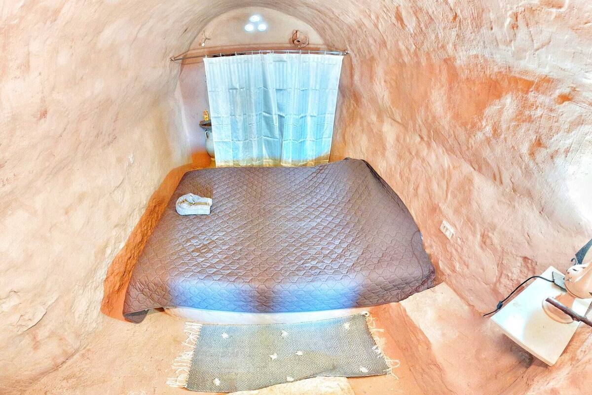 Une pièce étroite et voûtée, avec un lit, une petite table et un rideau.