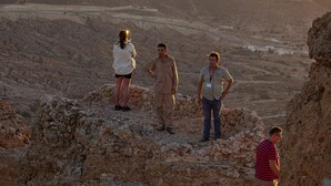 Trois personnes se tiennent debout sur un terrain rocheux, avec un paysage montagneux en arrière-plan.