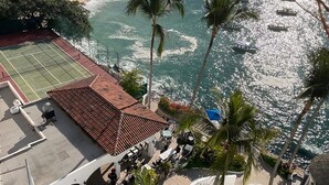 Vista con playa, cancha de tenis, palmeras y un edificio con terraza.