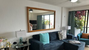 Una sala de estar con un sofá azul oscuro, una mesa de centro de vidrio y un espejo grande en la pared.