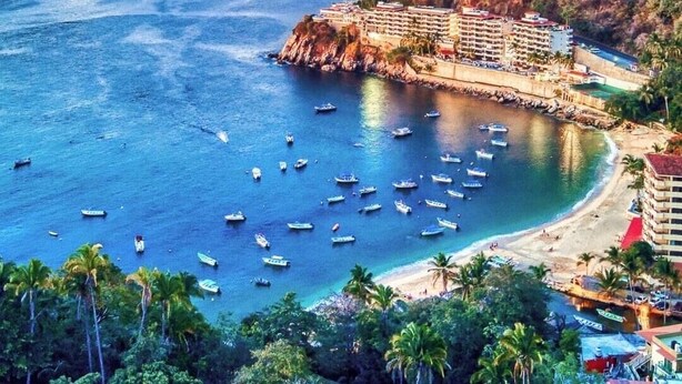 Un complejo turístico costero con varias edificaciones, una playa y barcos en el agua.