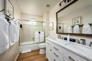 Een moderne badkamer met een douchecabine van glas, een grote spiegel en witte handdoeken aan haken.