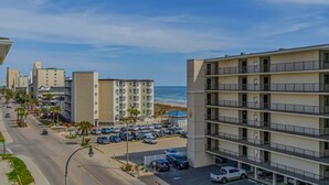 Um hotel com vários andares, varandas, estacionamento e vista para a praia.