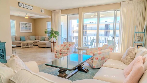 Uma sala de estar com sofá, poltronas, mesa de centro e varanda com vista.