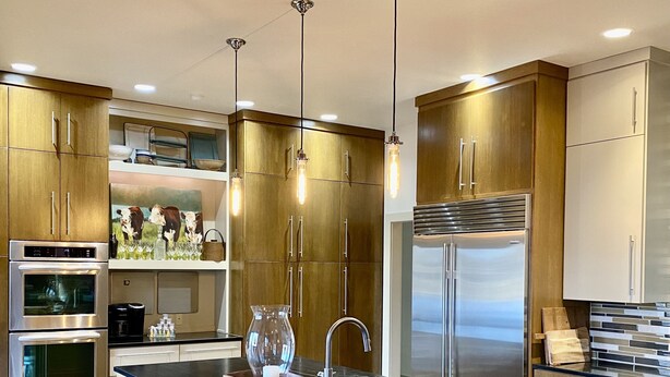 Une cuisine moderne avec des meubles en bois, des appareils en acier inoxydable, un îlot central doté de tabourets et un éclairage suspendu.
