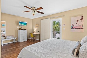 Une chambre à coucher comprenant un lit, un bureau, une chaise, un ventilateur de plafond et un téléviseur.