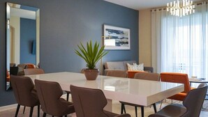 A modern living room with a large white table, brown chairs, a potted plant, a framed picture on the wall, and a chandelier. - Amazing 3 bedrooms condo in Resort with Water Park (Davenport)