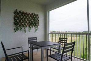 A balcony with a table and chairs, a lattice wall decoration, and a view of a green field.