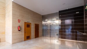 A modern elevator area with wooden doors, a fire extinguisher, and a metallic wall with horizontal lines. - Holidays2Malaga Eslava in a closed Urbanization (Málaga)