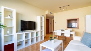 A modern living room with a flat-screen TV, white furniture, and a dining area with a kitchen in the background. - Holidays2Malaga Eslava in a closed Urbanization (Málaga)