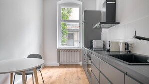 A modern kitchen with a white table, grey cabinets, and a window with a view of greenery. - Trendy Prenzlauer Berg 1BR, nr Mauerpark, by Blueground (Berlin)