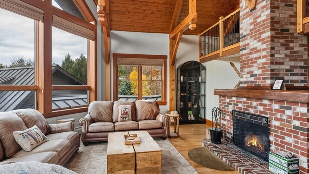 Un salón acogedor con chimenea, sofás de cuero y un ventanal grande con vistas a un paisaje nevado.