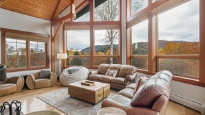Amplia sala de estar con ventanas grandes, techo de madera y mobiliario de cuero.